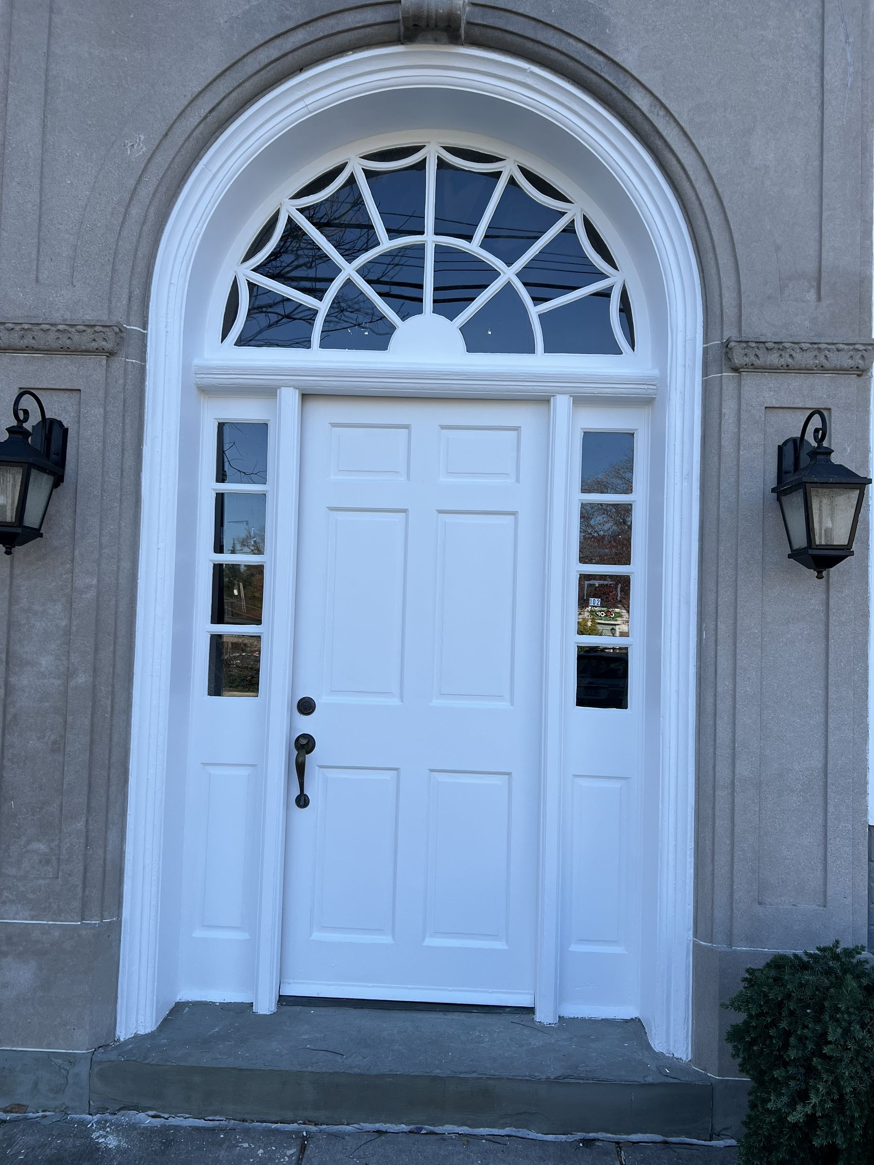 Freshly painted white front door with arched fanlight window and sidelights on a stone Philadelphia home